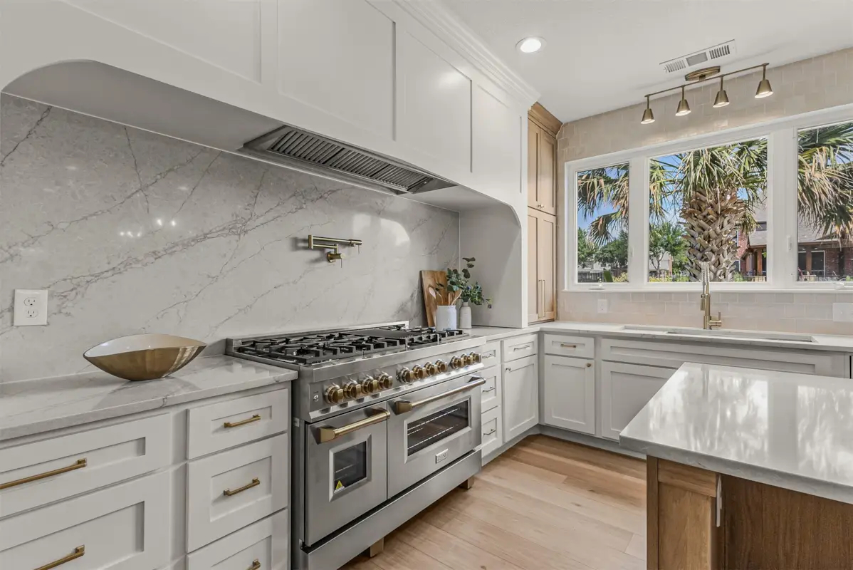 Modern luxury kitchen with marble backsplash, stainless steel double-oven range, and white cabinetry in a Rockwall County home