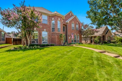Two-story red brick home with crape myrtles and manicured lawn