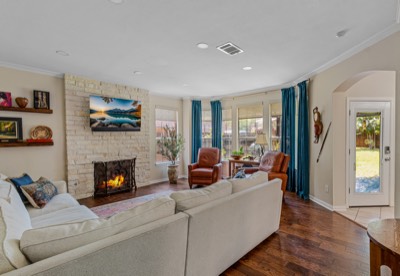 Living room with stone fireplace, wall-mounted TV, and bay windows to backyard