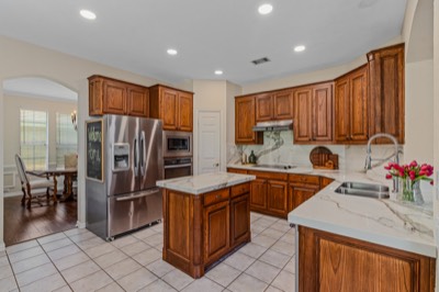 Kitchen with wood cabinets, marble counters, island, and stainless refrigerator