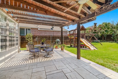 Pergola-covered stone patio with dining set overlooking backyard