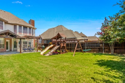 Backyard lawn with swing set and slide beside covered patio