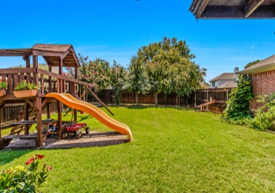 Wooden play structure with slide in green fenced backyard